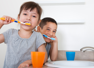 2 kids brushing teeth at sink with orange and blue cups