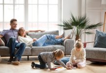 Children sister and brother playing drawing together on floor while young parents relaxing at home on sofa, little boy girl having fun, friendship between siblings, family leisure time in living room